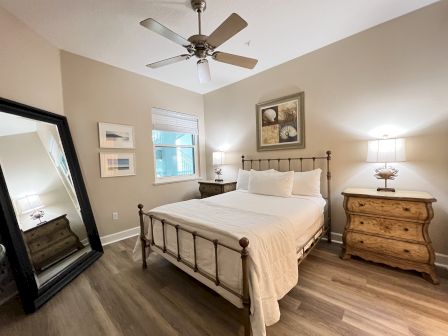 A cozy bedroom with a metal-framed bed, two wooden nightstands with lamps, a large mirror, and artwork on the walls.