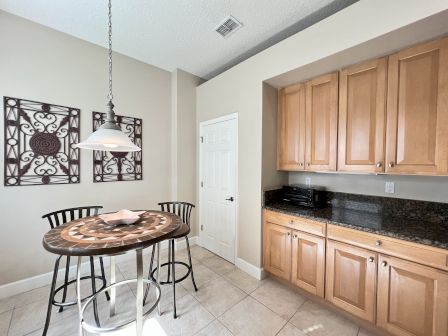 A kitchen corner with light wood cabinets, a table and chairs, decorative wall art, and a hanging lamp.