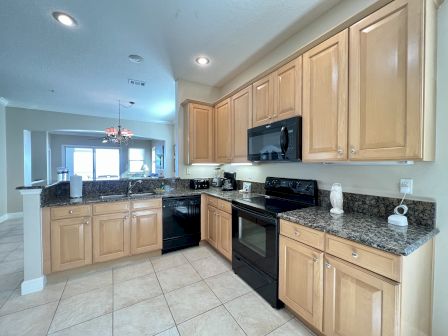 A kitchen with wooden cabinets, granite countertops, black appliances, and tile flooring. It overlooks a dining area.