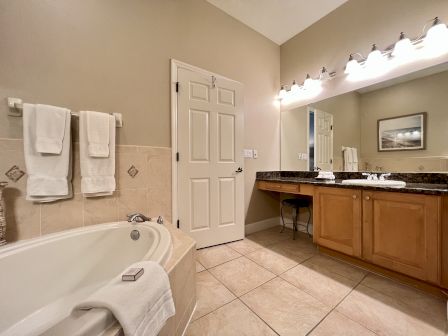 A bathroom with a bathtub, folded towels, a large mirror, lights, and a wooden vanity cabinet.