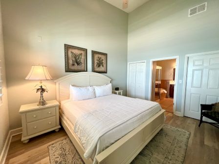 A bedroom with a bed, two framed art pieces, a lamp on a nightstand, and an open door leads to a bathroom.