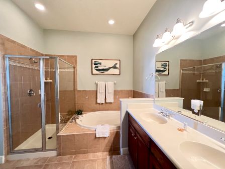 The image shows a bathroom with a glass shower, a bathtub, double sinks with a large mirror, and wall art.
