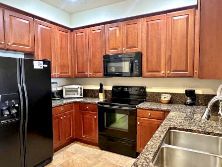 A kitchen with brown cabinets, black appliances, granite countertops, a double sink, and small appliances such as a toaster and coffee maker.