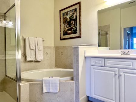 A bathroom with a bathtub, shower, sink, white cabinets, towel rack, and a framed painting on the wall.