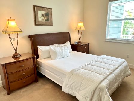 A cozy bedroom with a neatly made bed, flanked by two wooden nightstands with lamps. A framed artwork hangs above the bed.