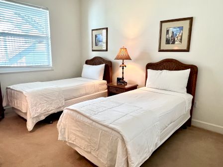 A tidy room with two twin beds, white bedding, a bedside table with a lamp, and framed artwork above each bed.