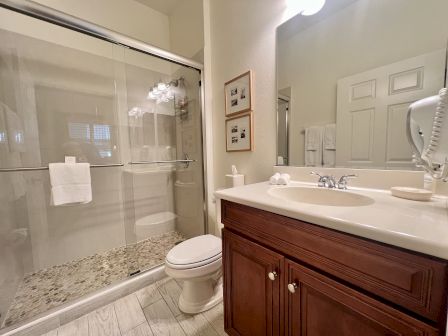 A bathroom with a glass shower, toilet, sink with a mirror, and wooden cabinets. Towels and a hairdryer are also visible.