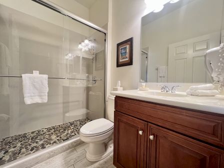 A bathroom with a stone-tiled shower, wooden cabinet, towels, and a large mirror above the sink.