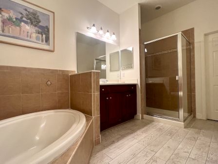 A bathroom featuring a bathtub, glass shower, vanity with mirror and lights, tiled floor, and wall art.