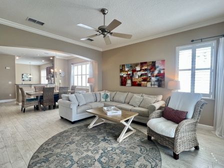 A cozy living room with a beige sofa, wicker chair, colorful abstract art, wooden coffee table, and a dining area in the background.