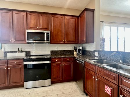 A kitchen with wooden cabinets, granite countertops, a stainless steel stove and microwave, a dishwasher, and a double sink.