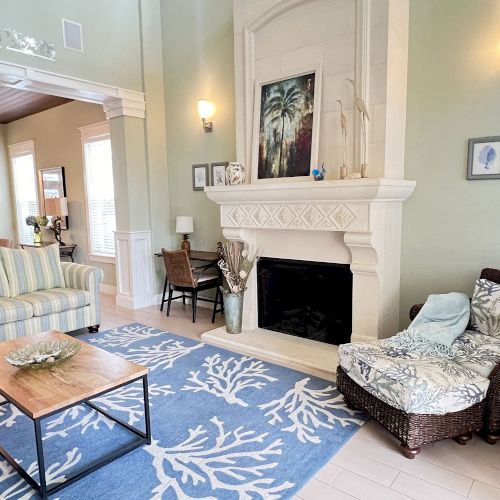 A cozy living room with a fireplace, striped sofa, wicker chair, and a blue rug with a white coral pattern.