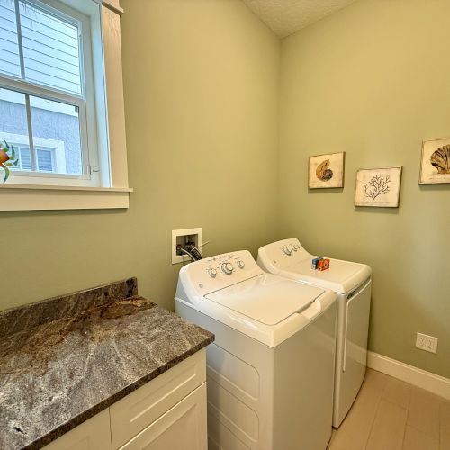 A laundry room with a washer and dryer, a countertop, wall art, and a decorative crab by the window.