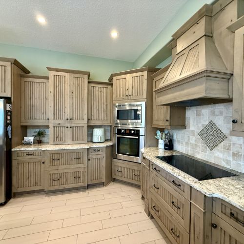 A kitchen with wooden cabinets, a stainless steel fridge, oven, countertop appliances, and tiled backsplash.