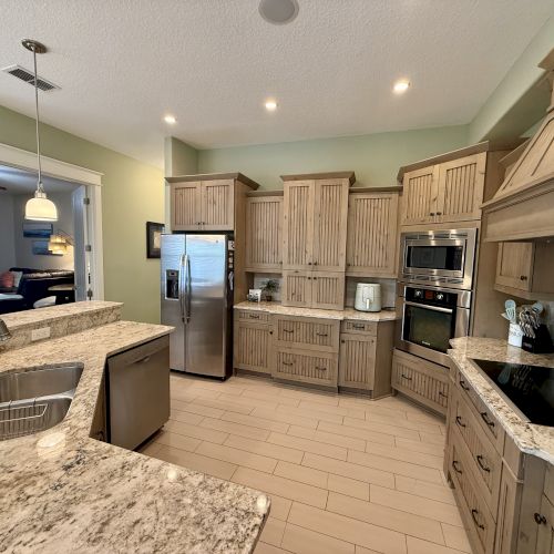 A modern kitchen with granite countertops, wooden cabinets, stainless steel appliances, and a view into a cozy living room.