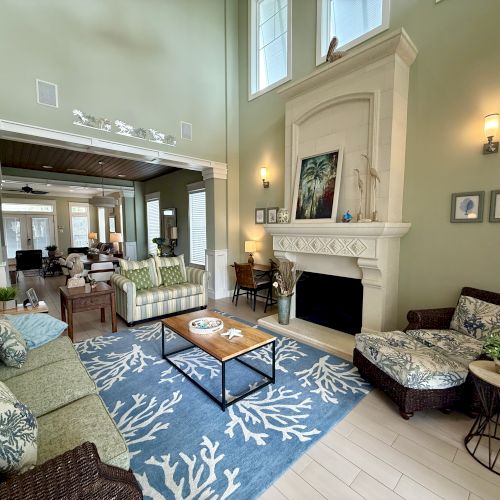 A cozy living room features green walls, a fireplace, sofas with patterned cushions, and a blue rug with white coral designs.