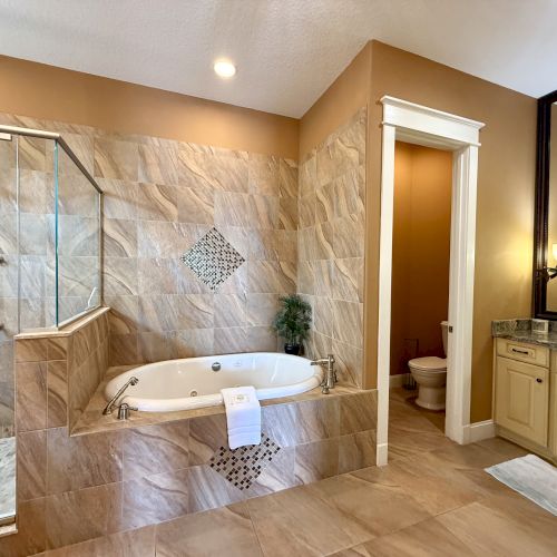 Luxurious bathroom featuring a glass shower, a jacuzzi tub with decorative tiles, a separate toilet area, and a large vanity with a mirror.