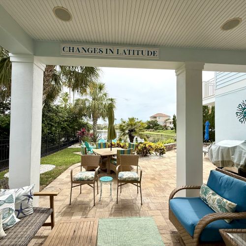 A patio with outdoor furniture, plants, a barbecue grill, and a sign reading "CHANGES IN LATITUDE" under a covered area.