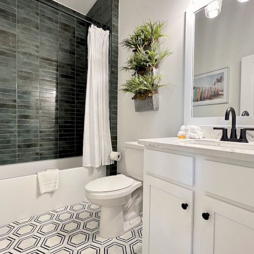 A modern bathroom features a green-tiled shower, white countertop, hexagonal floor tiles, and wall-mounted greenery for a fresh look.