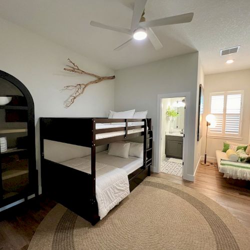 A cozy bedroom with bunk beds, a black cabinet, a round rug, and a sitting area near a bathroom.