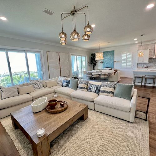 A modern open-concept living room and kitchen with a large sofa, stylish lighting, and a wooden coffee table on a woven rug.