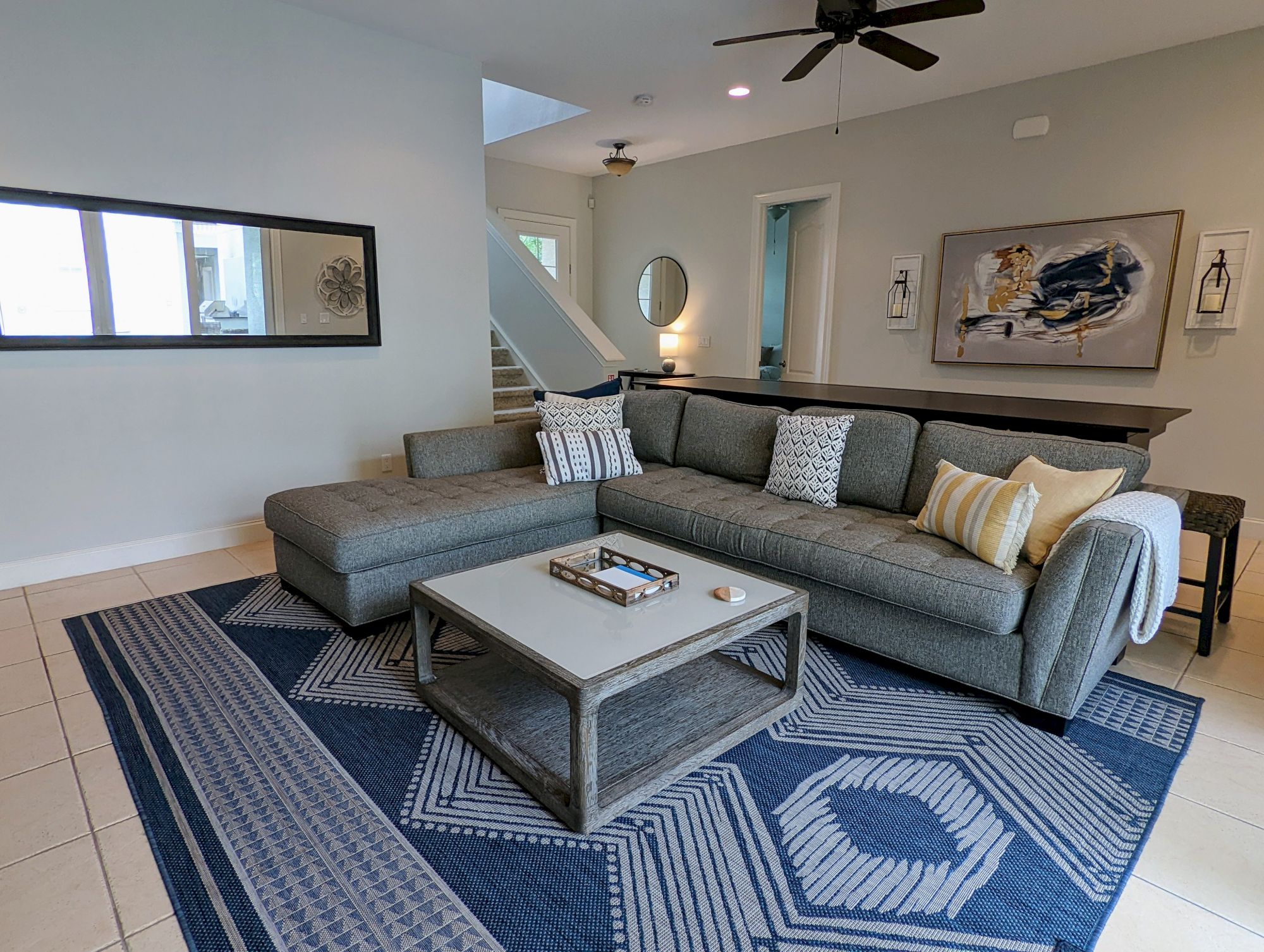 A modern living room with a gray sectional sofa, colorful cushions, a geometric rug, abstract art, and a ceiling fan.