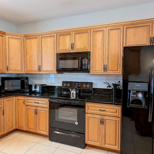 A kitchen with wooden cabinets, black appliances, a microwave, knife set, and countertop kettle is shown in the image.