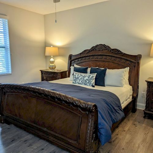 A cozy bedroom with a wooden bed, two nightstands, and table lamps, featuring a blue and white bedding set and hardwood flooring.