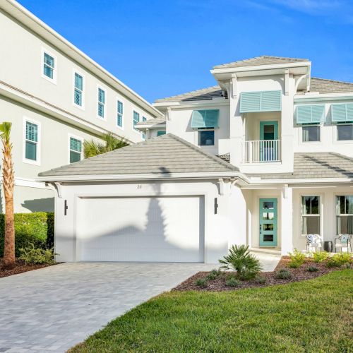 A modern two-story house with palm trees, a garage, and a well-maintained lawn under a clear blue sky.