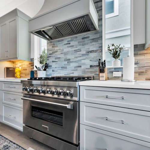 A modern kitchen with a stainless steel stove, tiled backsplash, white cabinets, and various kitchen items on the counter ending the sentence.