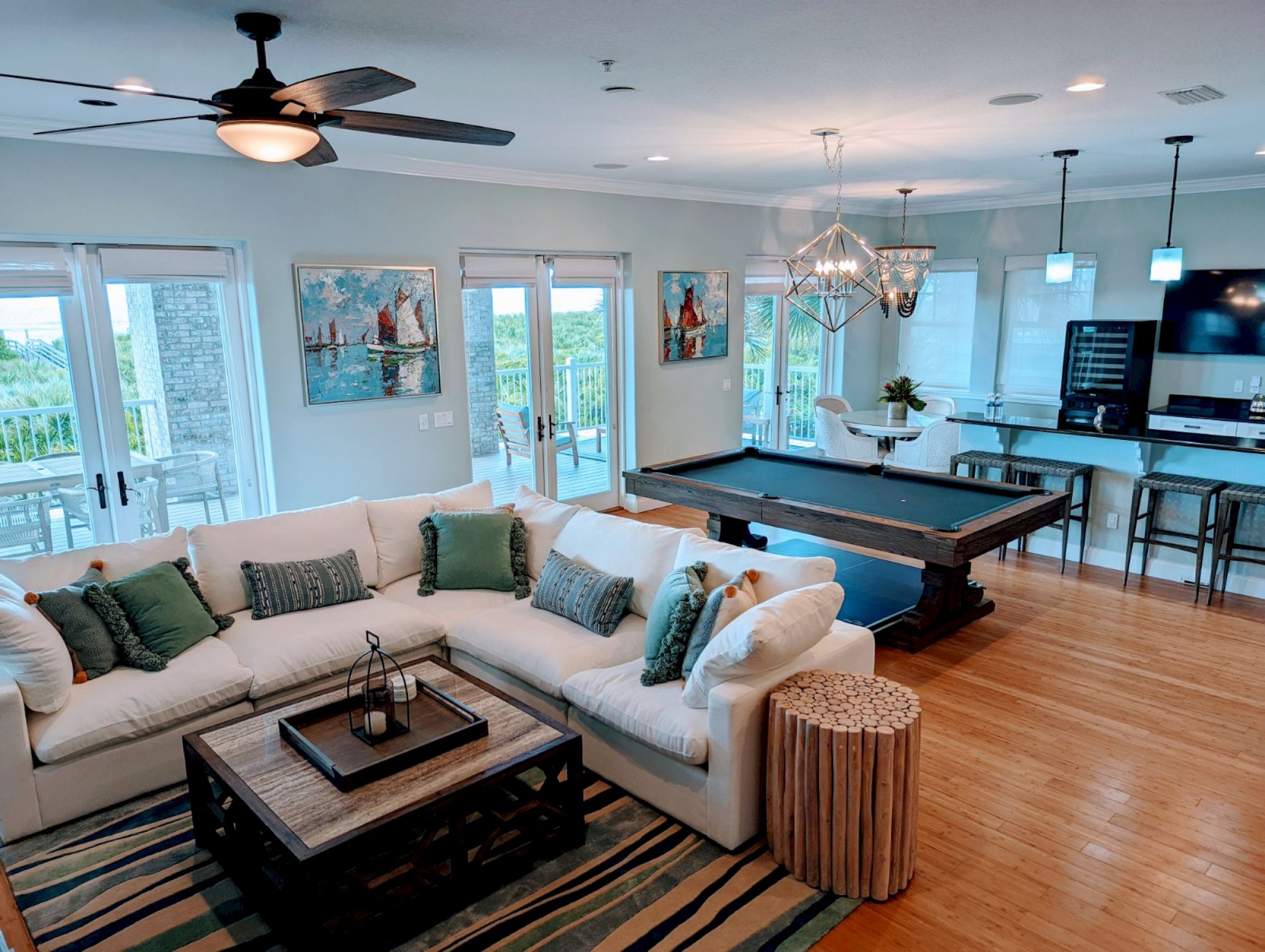 A spacious living area with a sectional sofa, pool table, kitchen with bar stools, ceiling fan, and large windows opening to a scenic view.