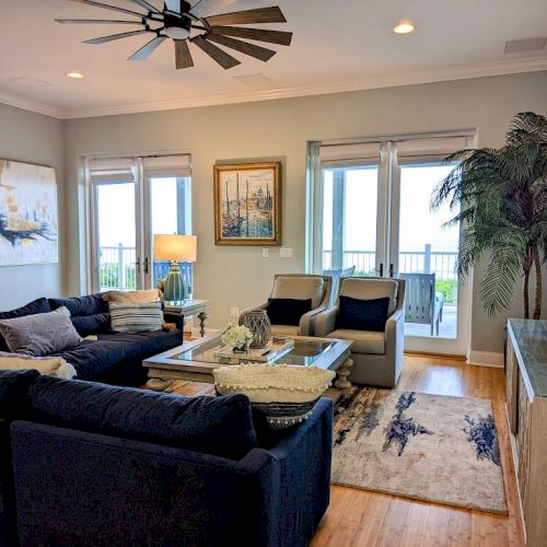 A cozy living room with a sectional sofa, chairs, decorative plants, artwork, and large windows revealing a balcony view.