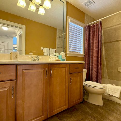 The image shows a bathroom with wooden cabinets, a mirror, a toilet, and a bathtub with a purple shower curtain.