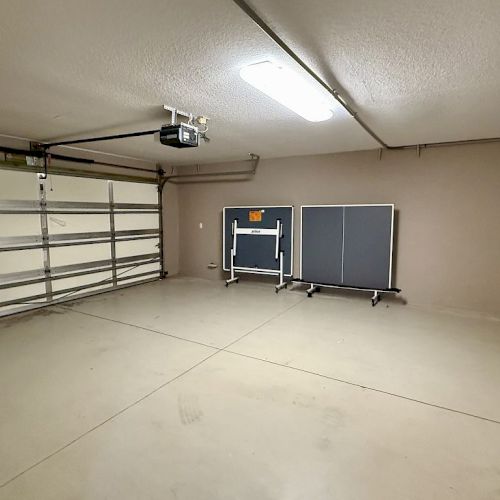 The image shows an empty garage with a ping pong table folded against the wall and a closed garage door.