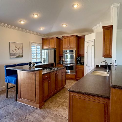 A spacious kitchen with wooden cabinets, an island, stainless steel appliances, and tiled flooring, offers a modern and functional look.