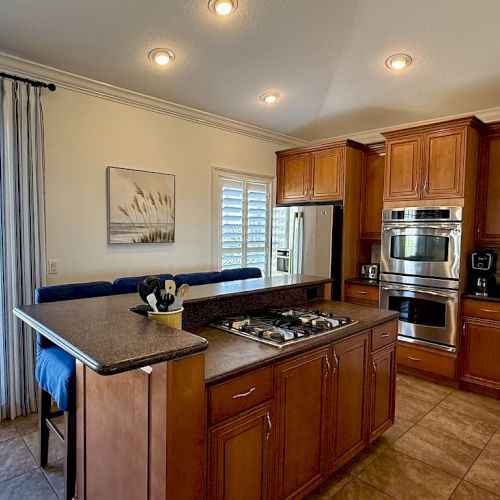 A modern kitchen with wooden cabinets, a central island with a stove, double ovens, and natural light from a window and glass door.
