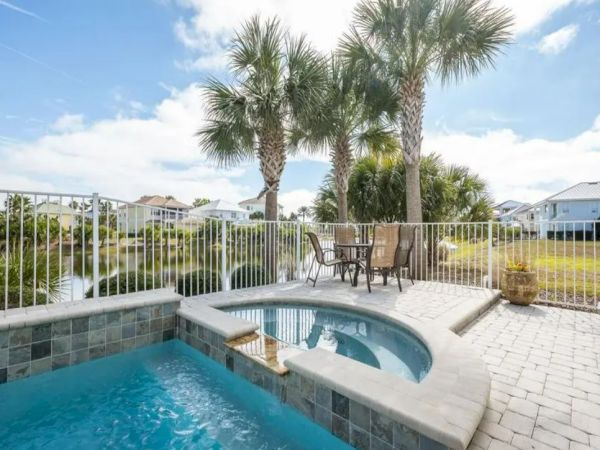 A serene patio with a pool and jacuzzi, surrounded by palm trees and a railing, overlooking a pond, and featuring a patio set.