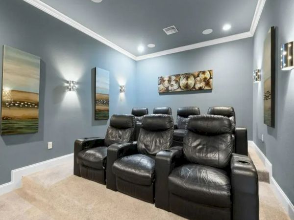 A home theater room with black leather recliners, paintings on the walls, and dim lighting.