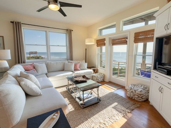 A cozy living room with a white sectional sofa, ocean view, and a TV cabinet with wooden floors complementing the bright space.