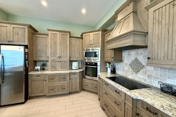 A kitchen with rustic wood cabinets, stainless steel appliances, granite countertops, and tiled backsplash.