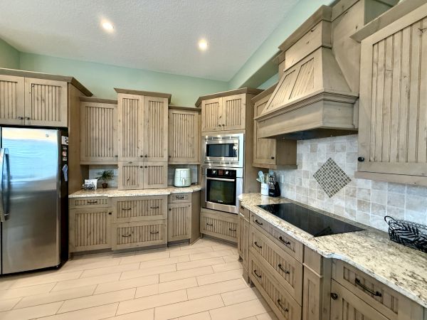A kitchen with rustic wood cabinets, stainless steel appliances, granite countertops, and tiled backsplash.