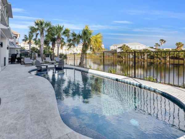 A serene poolside area with lounge chairs, palm trees, and a view of a fenced waterway in a residential setting.