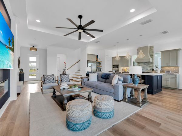 A modern living room and kitchen with a large TV, cozy seating, poufs, pendant lighting, and a wooden floor.