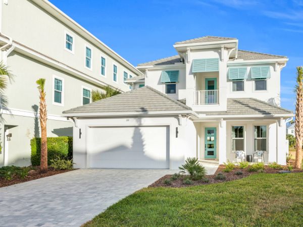 A modern two-story house with a garage, palm trees, and green lawn under a clear blue sky.