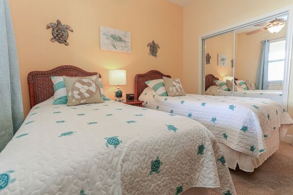 A bedroom with two twin beds, turtle-themed bedding, wicker headboards, and mirrored closet doors. Wall decor includes turtle art.