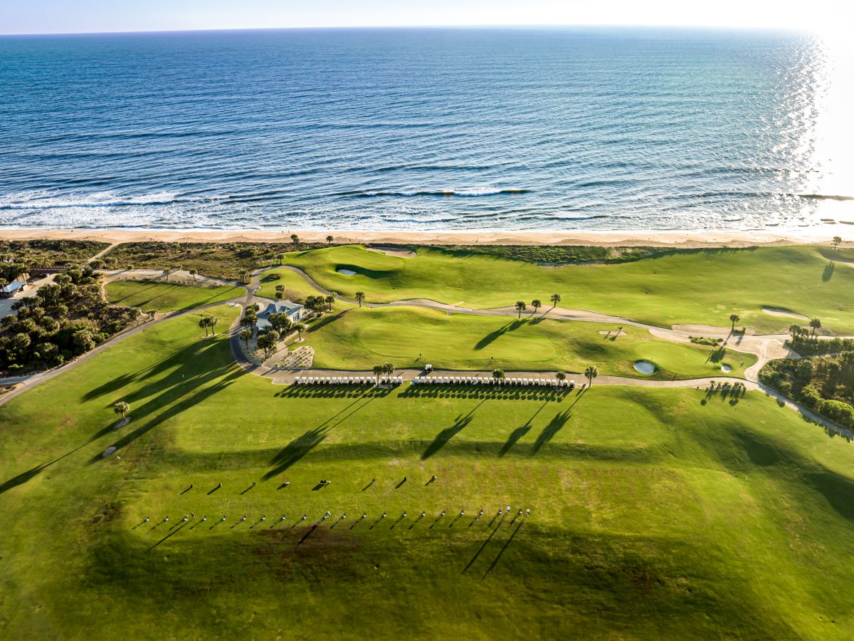 An aerial view of a golf course by the ocean, featuring greens, sand traps, and ocean waves meeting the shoreline.