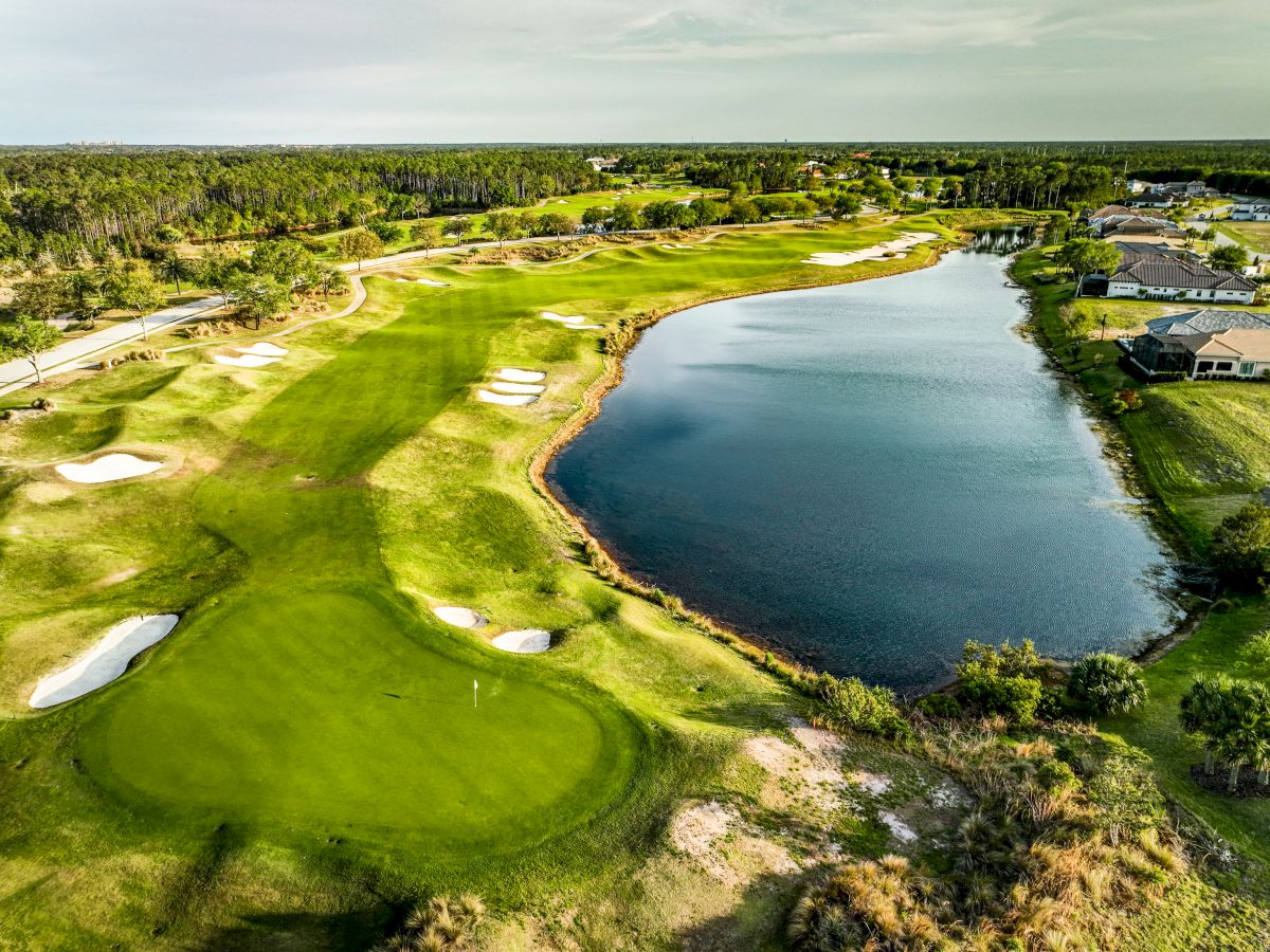 An aerial view of a golf course with green fairways, sand bunkers, and a large lake, surrounded by trees and buildings.