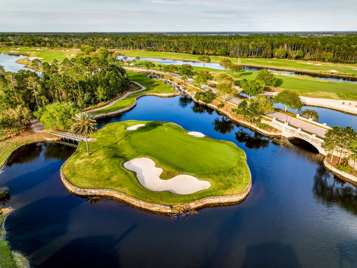 The image shows a scenic golf course with a green island hole surrounded by water, trees, and a bridge in a lush landscape.