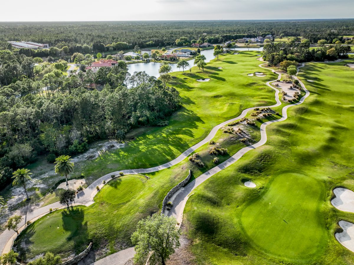 Aerial view of a picturesque golf course with winding paths, lush greenery, water features, and trees in the background.