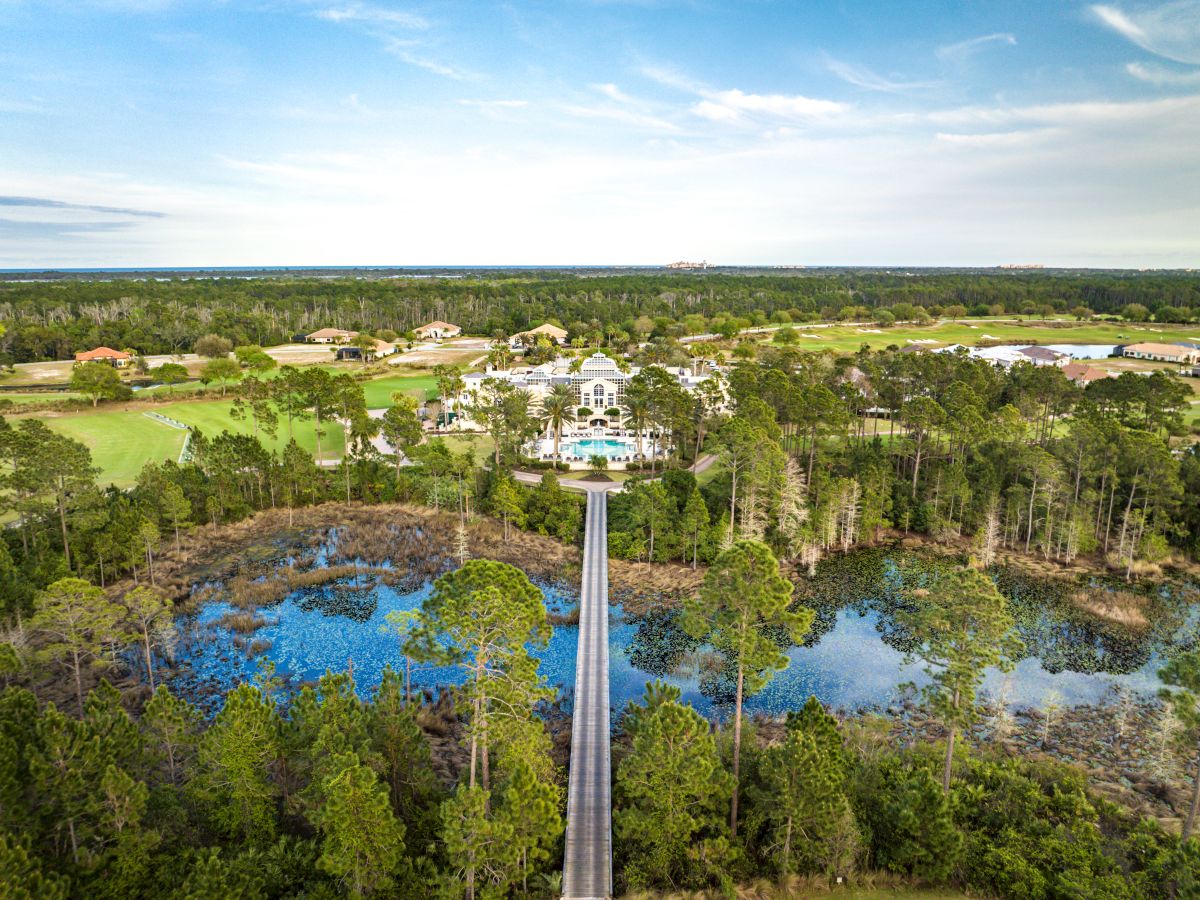 Aerial view of a large estate with a central mansion, surrounded by trees, water features, and a long pathway leading to the entrance.